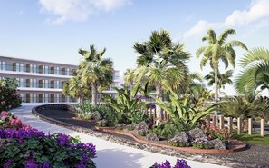 Un bâtiment moderne doté de nombreux balcons, entouré d’un aménagement paysager tropical comprenant des palmiers et des fleurs violettes.