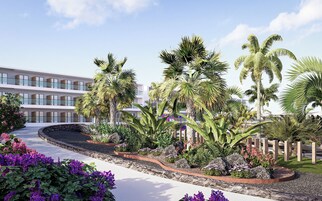 Un edificio moderno con varios balcones, rodeado de jardines tropicales con palmeras y flores moradas.