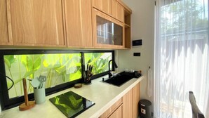 A kitchen with wooden cabinets, a black countertop, a window with a view of greenery, and a trash bin. - Terra House B1 (Kedonganan)