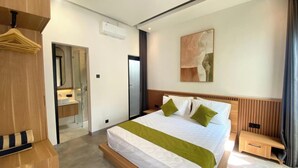 A hotel room with a bed, a bedside table, a mirror, a wardrobe, and a bathroom with a shower. - Terra House B1 (Kedonganan)