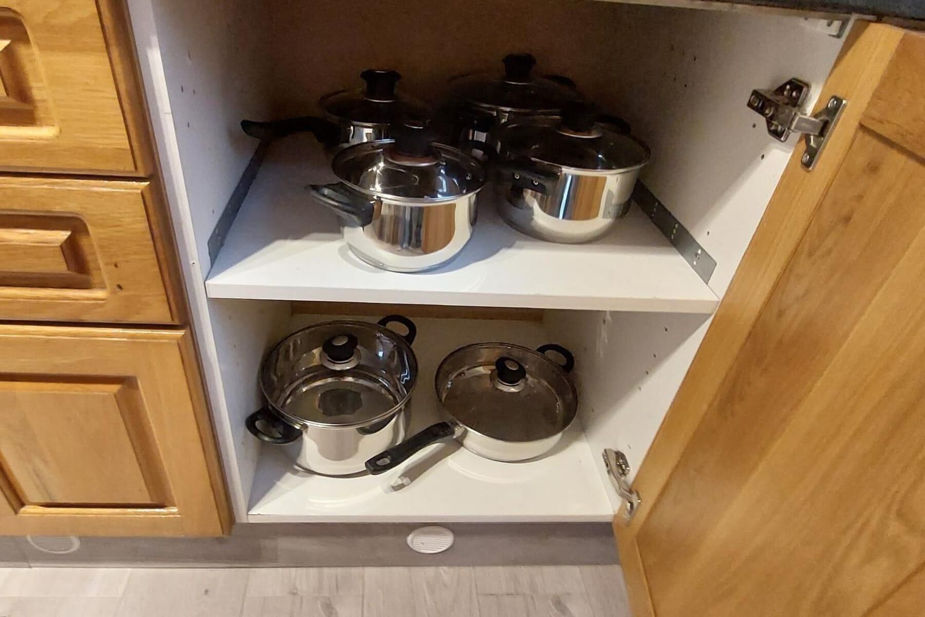 A kitchen with wooden cabinets and two shelves holding stainless steel pots and pans.