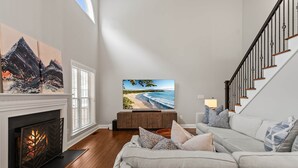 Ein Wohnzimmer mit Kamin, großem Fernseher, einer Couch und einer Treppe.