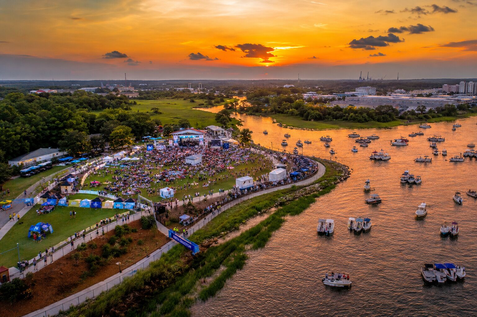 An aerial view of a riverside festival with boats and tents.