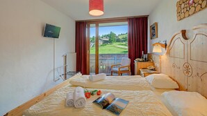 Habitación de hotel con cama, sillón, televisor, ventana con cortinas y vistas al exterior.