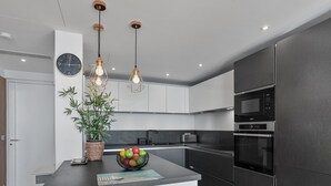Una cocina moderna con una isla central, electrodomésticos de acero inoxidable, iluminación colgante y un reloj en la pared.