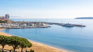 Una marina con barcos amarrados, una playa de arena y edificios al fondo.