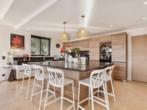 A modern kitchen with a large island, white bar stools, wooden cabinets, and pendant lighting. - Sea View • Pool • Near Saint-Tropez (Sainte Maxime)