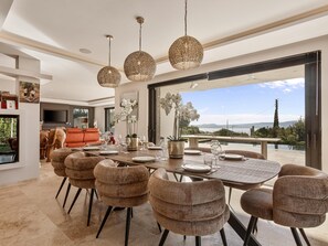 A dining area with a large table set for six, surrounded by upholstered chairs, with a view of the outdoors. - Sea View • Pool • Near Saint-Tropez (Sainte Maxime)