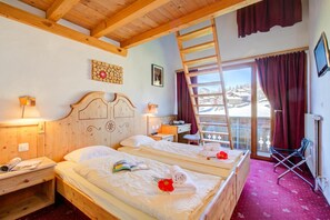 Une chambre d’hôtel avec deux lits, un plafond en bois, une fenêtre donnant sur un paysage enneigé, un bureau avec une chaise et un téléviseur fixé au mur.