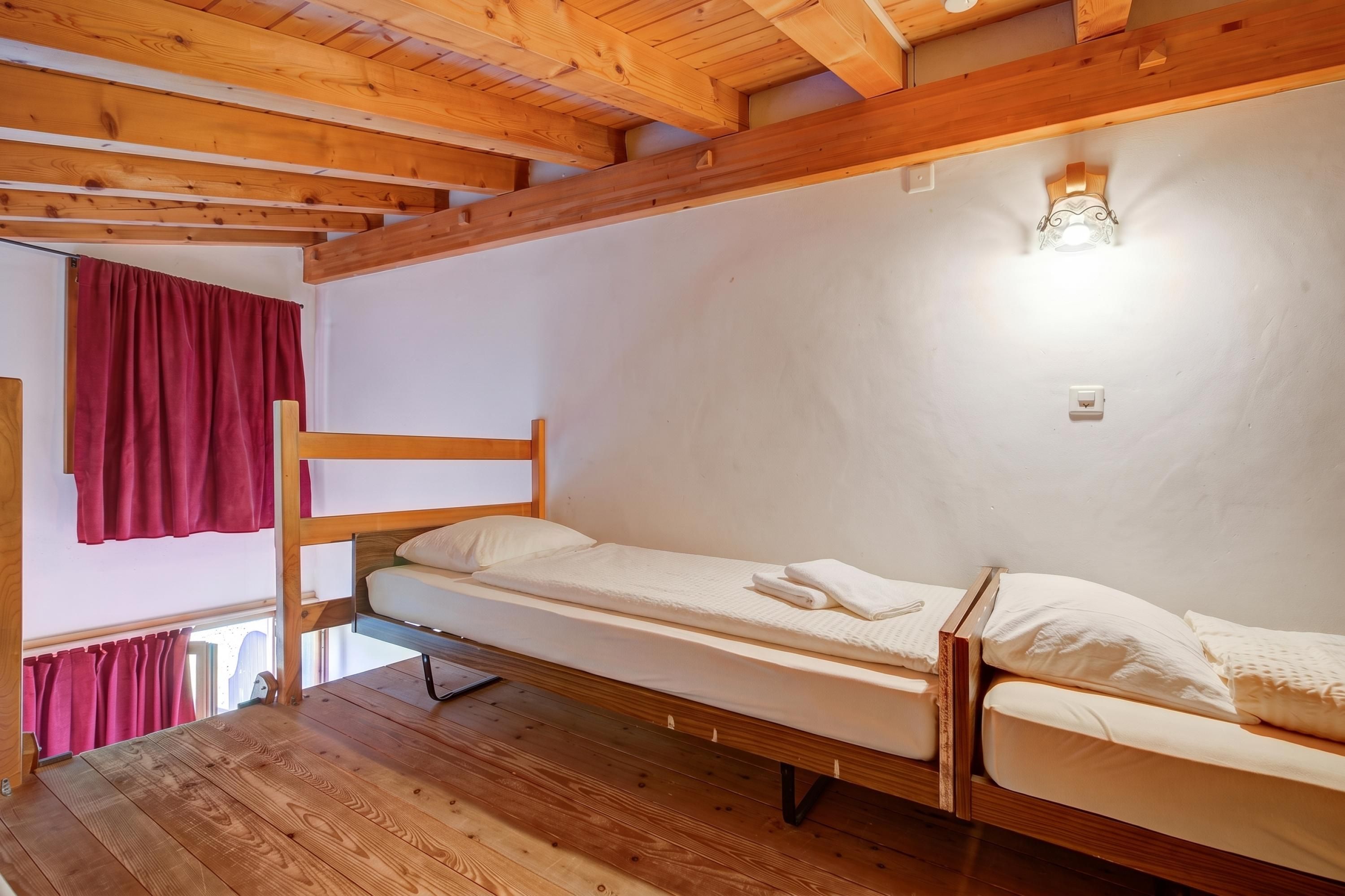 Una cama litera en una habitación con vigas de madera en el techo y una pared blanca.