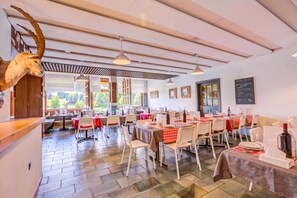 Un restaurant doté de nombreuses tables, de chaises et d’un plafond avec des poutres apparentes.