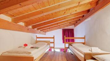 Ein Zimmer mit Holzbettställen, Holzboden und einem Fenster mit Vorhängen.