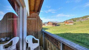 Un balcon avec une balustrade en bois, deux chaises en plastique blanches et une table avec des tasses.