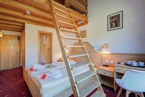 Eine Holzleiter führt zu einem Schlafbett auf Podest, ein Holztisch mit Stuhl und ein Wandbild.