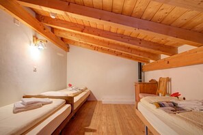 Ein Zimmer mit zwei Einzelbetten, Holzbalken an der Decke, einem kleinen Tisch und einem Stuhl.