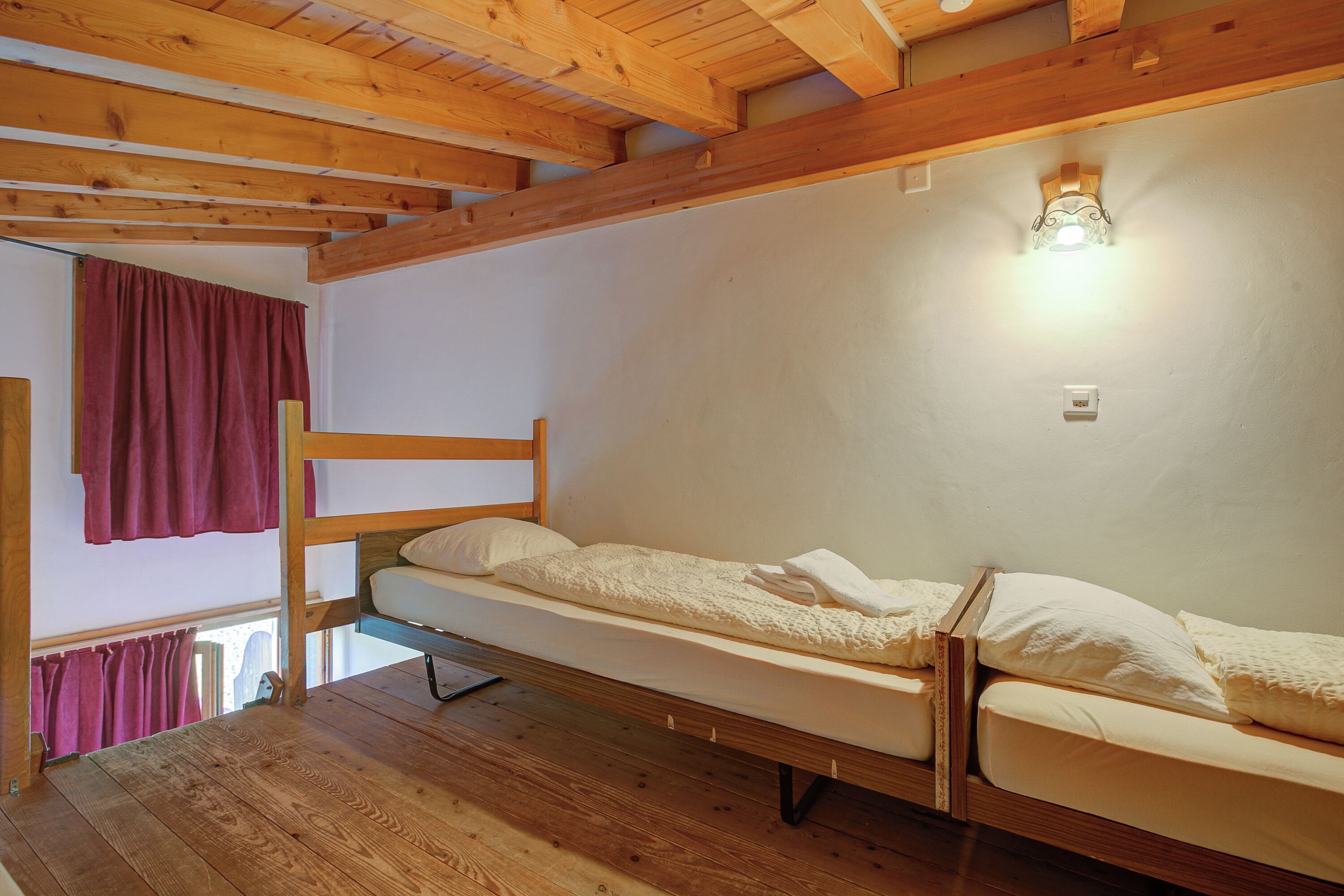 Una cama litera de madera con colchón y almohadas blancos, techo de madera y una pequeña lámpara en la pared.