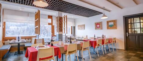 Ein Restaurant mit mehreren Tischen, Stühlen und Blick auf verschneite Berge durch große Fenster.
