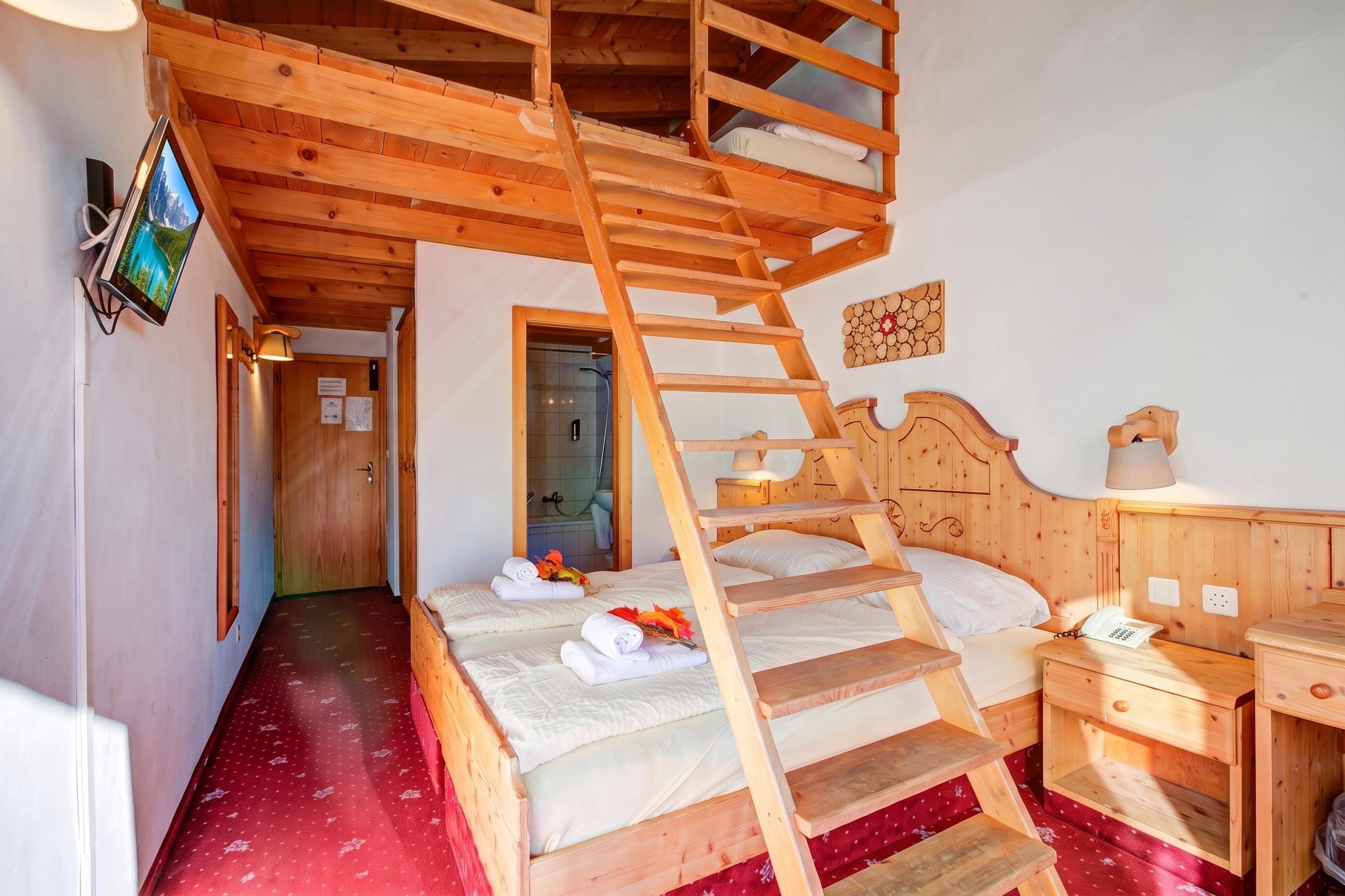 Una habitación de madera con literas, una escalera de madera, una mesita de noche, una lámpara de pared y una pequeña mesita con lámpara.
