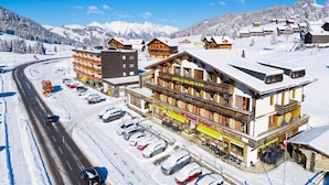 Un hotel con un telesilla, paisajes nevados y una carretera con coches estacionados.