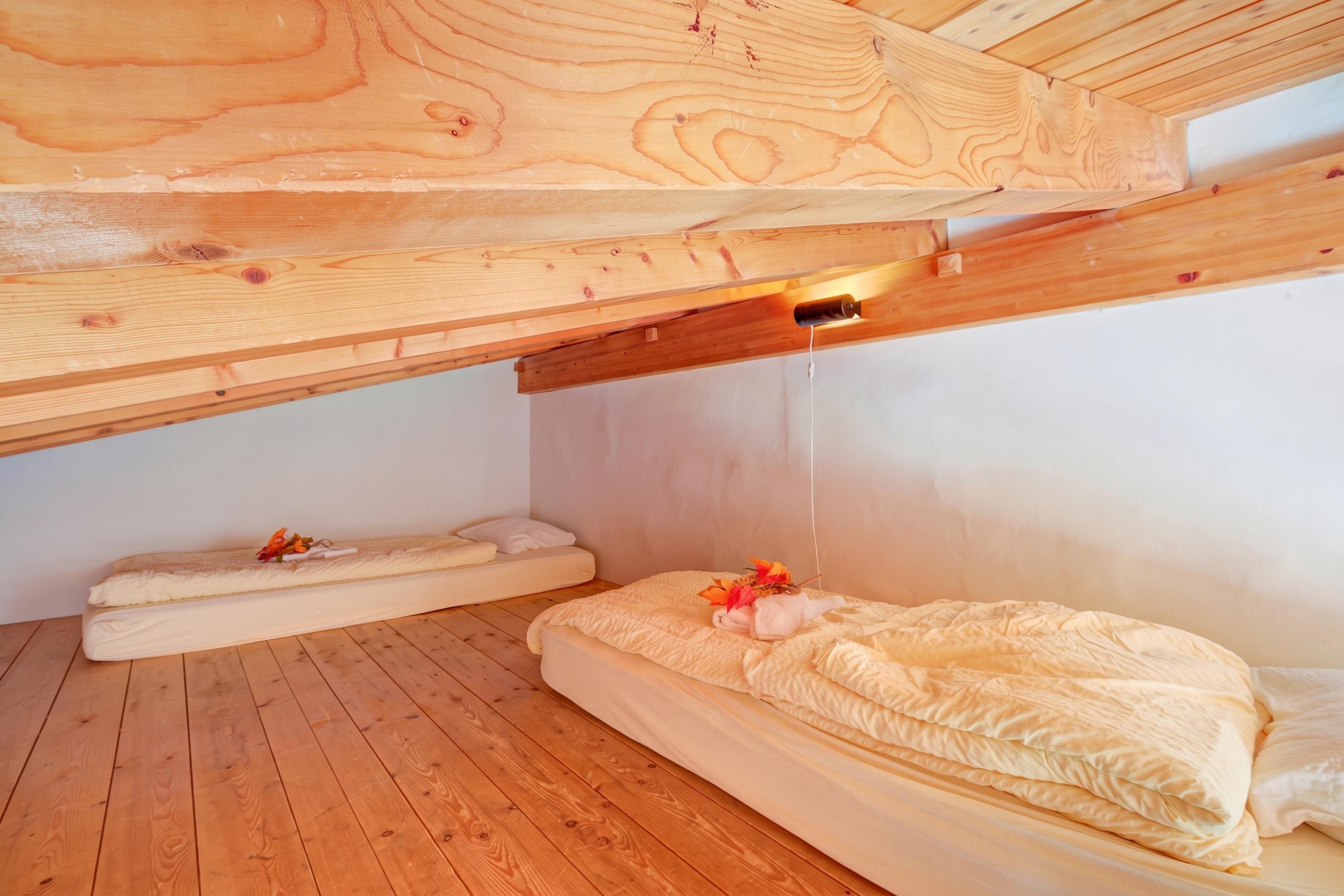 Habitación con pisos de madera y techo inclinado, con dos camas vestidas con ropa blanca y un adorno en una de ellas.