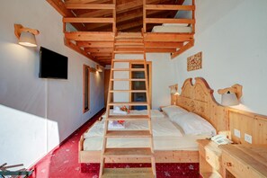 Un lit superposé en bois avec une échelle, une table de chevet avec une lampe, un téléviseur à écran plat et un sol recouvert d’une moquette rouge.