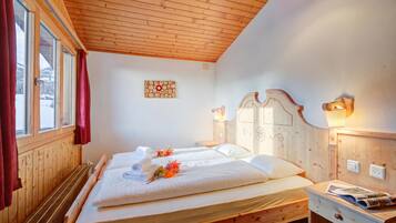 Una habitación de madera con una cama, un ventanal con cortinas, una lámpara de pared y una mesita con una revista.