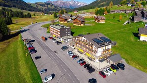 Ilmakuva hotellista, jossa on useita rakennuksia, parkkipaikka ja vuoristomaisema taustalla.