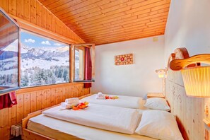 Ein Holzhütten-Zimmer mit einem Bett, einem Fenster mit Blick auf schneebedeckte Berge und einer Wandleuchte.