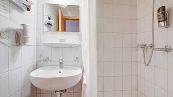 Ein Badezimmer mit einem weißen Waschbecken, einem Spiegel und einer Dusche. An der Wand befinden sich ein Handtuchhalter und eine Shampooflasche.