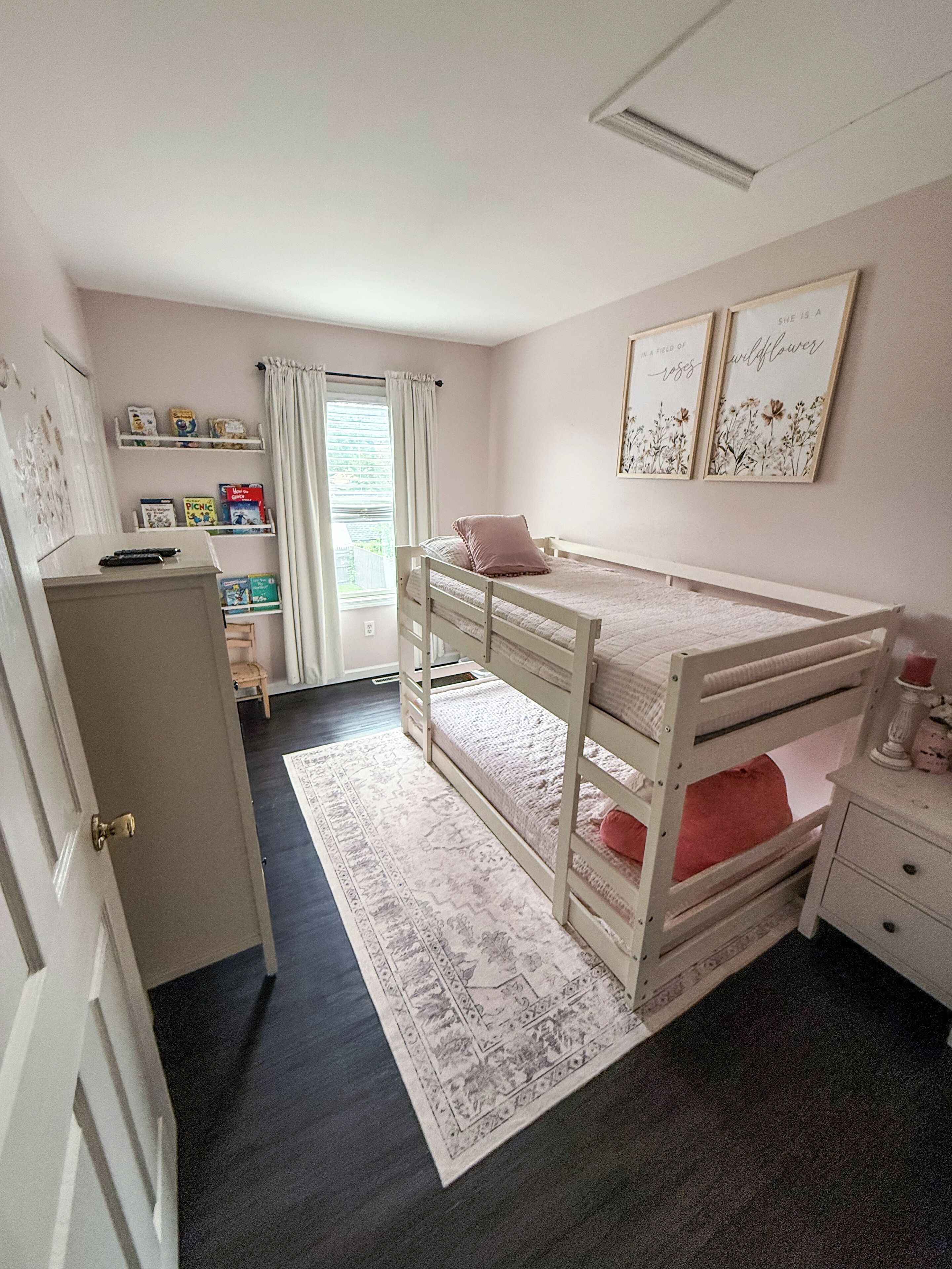 Une chambre d’enfant avec des lits superposés, un bureau, des étagères remplies de livres et une fenêtre avec des rideaux.