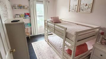 Une chambre d’enfant avec des lits superposés, un bureau, des étagères remplies de livres et une fenêtre avec des rideaux.