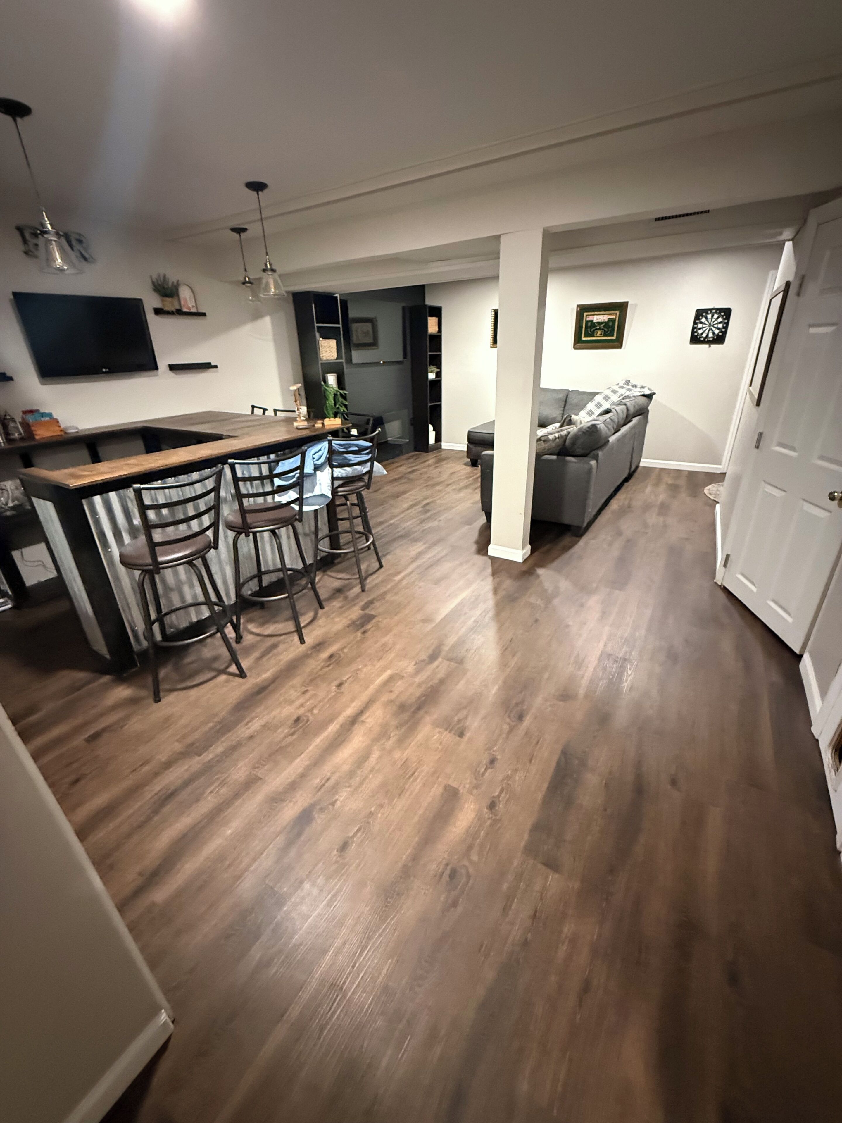Un vaste espace de vie doté d’un plancher en bois, d’un coin bar avec des tabourets, d’un canapé et d’un téléviseur fixé au mur.