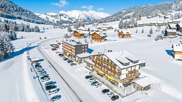 Un paese montano imbiancato dalla neve, con edifici in legno, una seggiovia e un'area di parcheggio.
