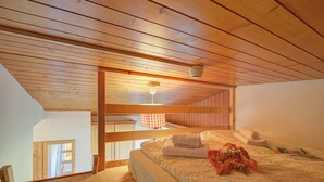 Slaapkamer met houten balken, een bed met handdoeken, een raam en een plafondlamp.