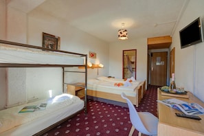 Habitación de hotel con literas, un escritorio con silla, un televisor y una mesita con una botella y vasos.