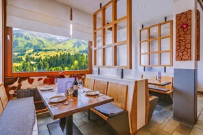 Un comedor con una mesa dispuesta para dos, vista a colinas verdes a través de ventanas amplias y decoración de pared de piedra.