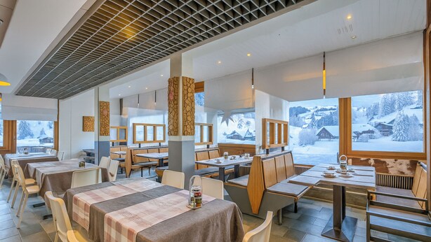 Un restaurante con varias mesas y sillas, amplias ventanas con vistas a montañas nevadas y un diseño moderno en el techo.