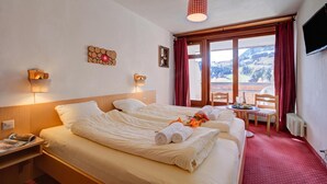 Ett hotellrum med två sängar, ett matbord, stolar, en TV och ett fönster med utsikt över bergen.