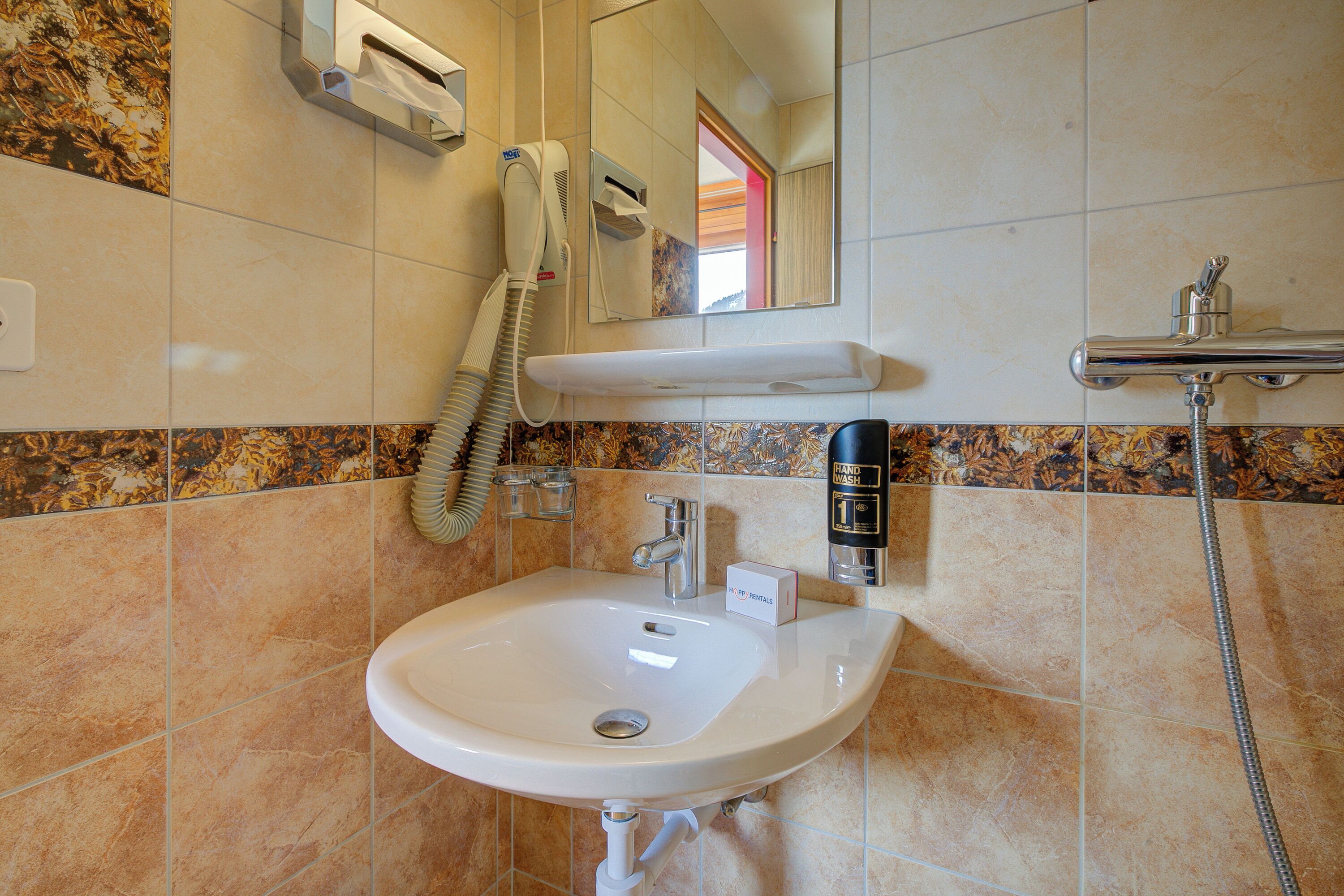 Een badkamer met een wastafel, spiegel, haardroger en handdroger.