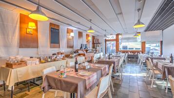 Ein Restaurant mit mehreren Tischen, Deckenleuchten und Blick ins Freie.