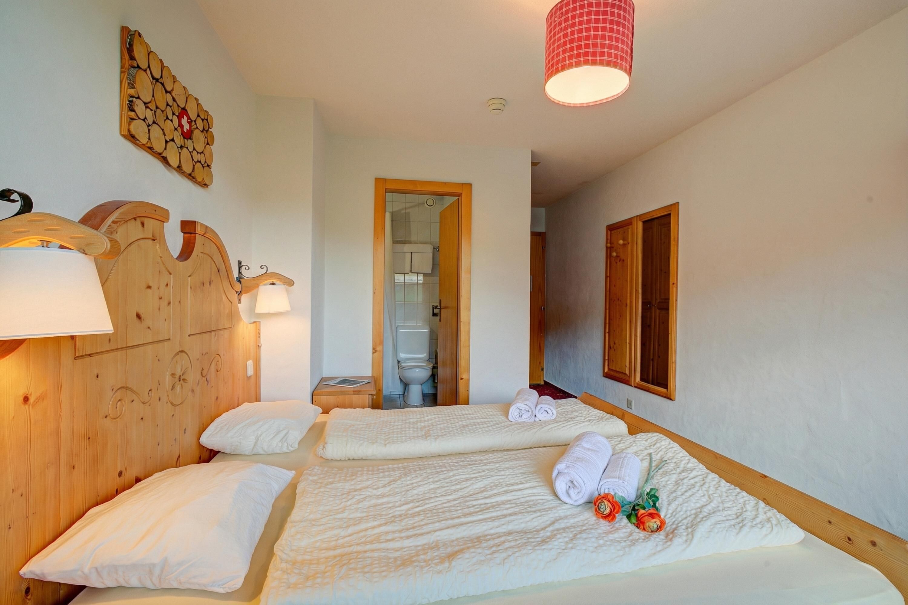 A hotel room with two beds, wooden headboards, a wooden wall decor, a red checkered lamp, and a wooden door.
