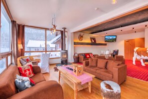 A spacious living room with a fireplace, comfortable seating, a television, and a large window with a view of a snowy landscape. - Hotel Relais Alpin Twin Room & Balcony4 231, Les Mosses, Switzerland (Les Mosses)