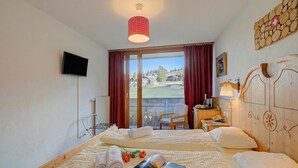 Habitación de hotel con dos camas, televisión, cabecero de madera, ventana con cortinas y vista al exterior.