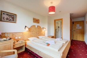 Habitación de hotel con cama de madera, mesitas de noche, un espejo, armario de madera y alfombra roja.