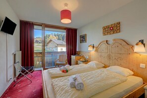 A hotel room with two beds, a TV, a red curtain, a wooden headboard, and a view of houses outside.