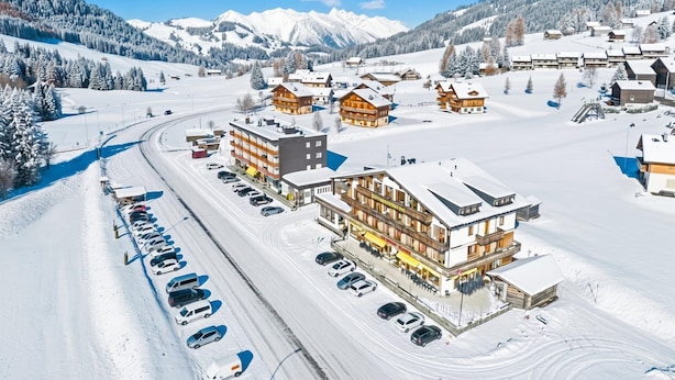 Un pueblo cubierto de nieve con edificios de madera, un telesilla y un estacionamiento.