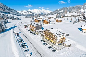 Un pueblo cubierto de nieve con edificios de madera, un telesilla y un estacionamiento.