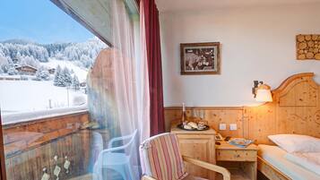 Ein Hotelzimmer mit einem hölzernen Bett, einem Nachttisch mit Lampe, einem Sessel und Blick auf schneebedeckte Berge.