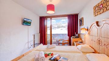 Ein Hotelzimmer mit zwei Betten, einem Fernseher, einem Holzschrank, einem Schreibtisch mit Lampe und Blick auf eine verschneite Landschaft.