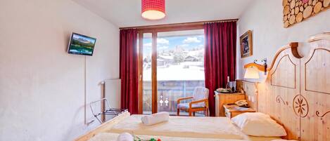 Ein Hotelzimmer mit zwei Betten, einem Fernseher, einem Holzschrank, einem Schreibtisch mit Lampe und Blick auf eine verschneite Landschaft.